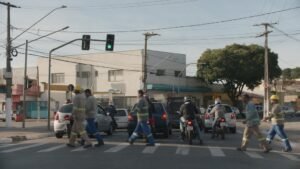 Esquina movimentada de cidade do interior no horário de pico, com carros, motos e pedestres no trajeto diário
